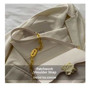 Detail of off-white leather bag with gold chain strap and textured buckle on a blazer