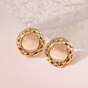 Close-up of vintage gold-rimmed button earrings with pink stone and lattice texture