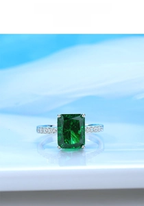 Macro shot of an emerald-cut green gemstone on a silver band with side accent diamonds
