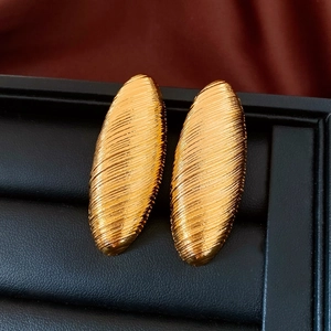 Détail de boucles d'oreilles dorées ovales avec finition en métal brossé horizontal