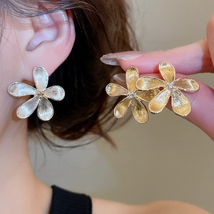 Dettaglio di orecchini a fiore in metallo spazzolato oro e argento su pelle