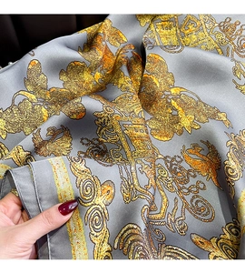 Detailed macro view of gray silk scarf featuring ornate golden baroque patterns and texture