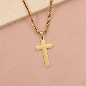 Detailed shot of a gold cross pendant with box chain on a minimalist textured surface