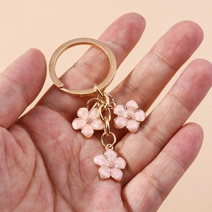 Hand holding golden keychain with three pink enamel cherry blossom floral charms
