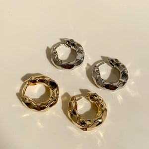 Detailansicht klobiger Creolen in Gold und Silber mit unregelmäßiger Metalltextur