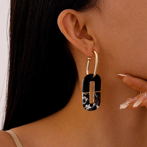 Macro view of geometric dark marble acrylic earrings on model's ear with golden metal details