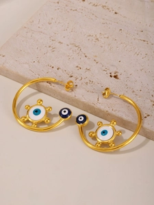 Close-up of golden evil eye C-shaped hoop earrings with blue enamel sunray details