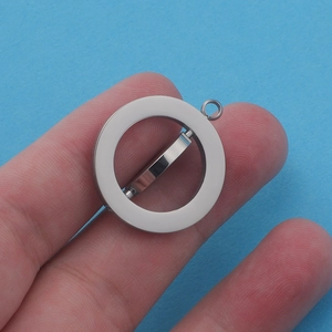 Mirror polished stainless steel spinning circle pendant held by hand on blue background