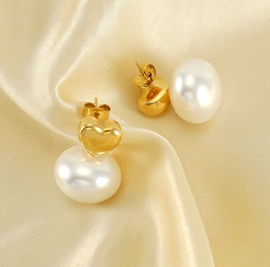 Detailed close-up of golden heart earrings with white pearls on champagne silk background