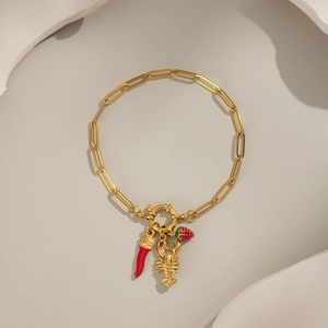 Gold paperclip chain bracelet with strawberry and chili pendants on minimalist background