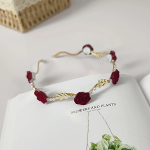 Elegant gold wavy headband with red rose and pearls displayed on an art book