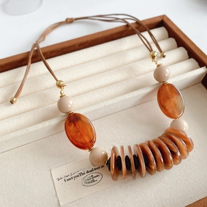 Detail of leather cord necklace with brown and beige beads on a wooden jewelry tray