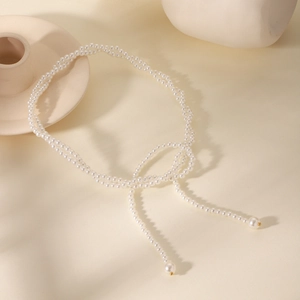 Detail of elegant white pearl lariat necklace draped over minimalist ceramic decor