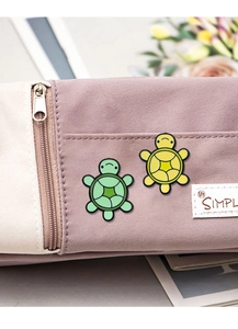 Close-up of cute green and yellow turtle enamel pins on a canvas pencil case