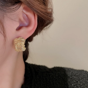 Close-up of gold irregular twisted cube earring on model with metallic texture details