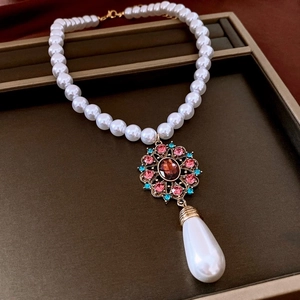 Detail of vintage flower pendant with red and blue gems and teardrop pearl on necklace
