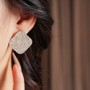 Close-up of a silver square earring with sparkling diamonds worn on model's ear
