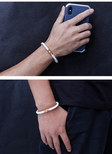 Detailed view of white braided leather bracelet with golden magnetic clasp on male model