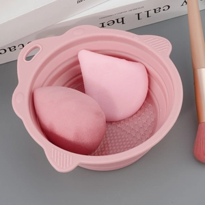 Pink silicone makeup brush cleaning bowl with two soft beauty sponges on a grey table