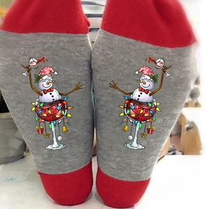 Christmas snowman socks with red wine glass and festive lights on gray fabric