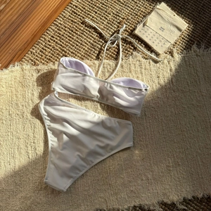 Flachbild des weißen Bandeau-Bikinis mit Metallblume auf einer gewebten Matte