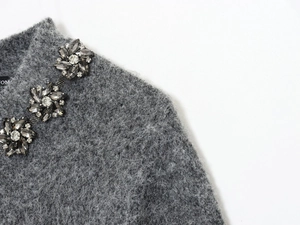 Dettaglio ricamo floreale in cristallo e catena su maglione in mohair grigio