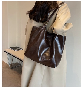 Detail of dark brown leather tote bag with glossy finish held by a model in a trench coat