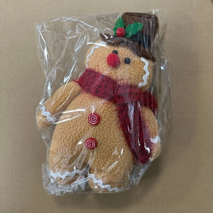 Detail of gingerbread man plush doll with red scarf and peppermint buttons in packaging