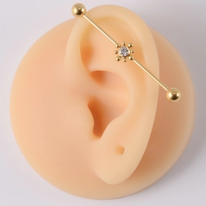Detailed view of golden industrial barbell earring with clear gem flower on silicone ear model