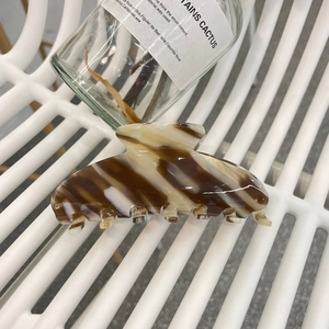 Detail of elegant brown and white striped acetate hair claw clip on a textured surface