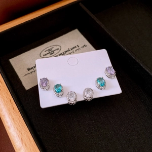 Three pairs of oval crystal stud earrings in purple, blue, and white on a display card