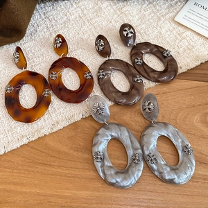 Detail of gothic acrylic earrings with chrome cross motif in amber and marble patterns