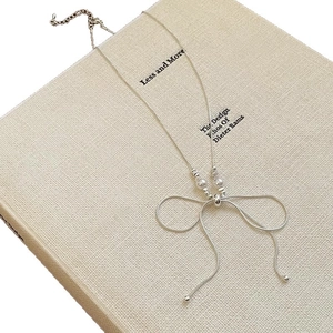 Silver bow pendant necklace with white pearls on a sleek snake chain over a book