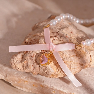 Detail view of pearl necklace with pink silk bow and heart-shaped gemstone on stone