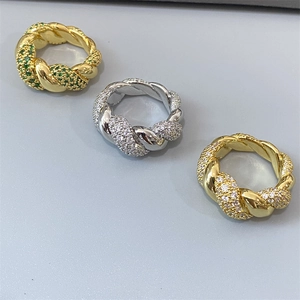 Detailed view of three twisted rings with green and clear gemstones on grey background
