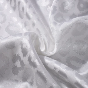 Gros plan d'un tissu satiné jacquard léopard blanc avec des reflets soyeux et nacrés