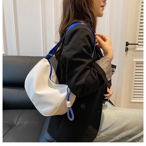 White crescent underarm bag with blue straps shown on model in a minimalist home setting