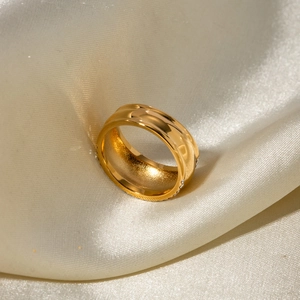 Detailaufnahme von vergoldetem Edelstahlring mit eingelegten Kristallen auf Satinstoff