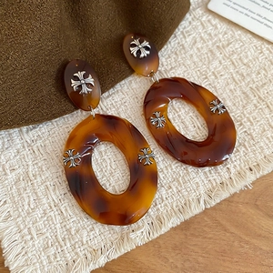 Close-up of tortoise shell resin drop earrings with vintage silver cross pendants