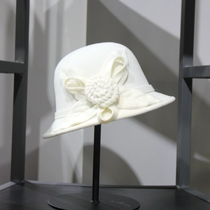 Detail of white wool cloche hat featuring a large 3D knitted flower on metal stand
