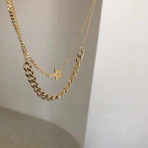 Detail of gold double-layer necklace featuring star pendant and mixed Cuban chain links
