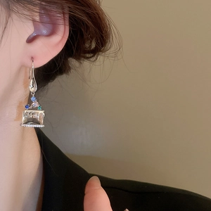 Vintage asymmetrical silver drop earrings with blue and green crystals on a model