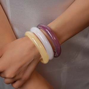 Detailed view of three resin bangles in yellow, white, and lilac worn by a model