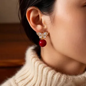 Elegant gold butterfly earrings with zircon inlay and red pearl pendants on model