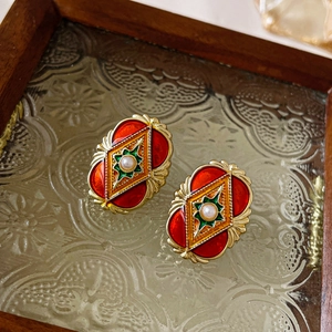 Macro detail of vintage geometric earrings with enamel and pearls on floral glass tray
