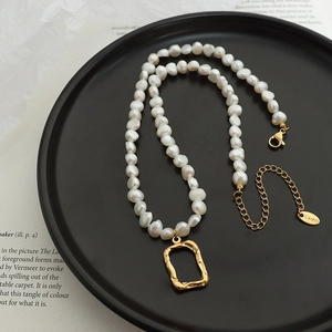 Baroque pearl necklace with a gold rectangle pendant on a matte black display plate