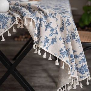 Detail of linen tablecloth with blue floral pattern and decorative tassel edge in a home setting