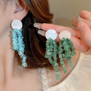 Detail view of long tassel earrings with blue and green stones on a model