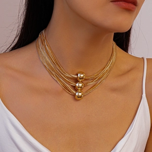 Detail of layered gold chain necklace featuring three polished spheres on neck model