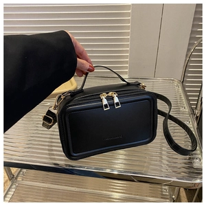 Detail of black rectangular crossbody bag with golden dual zippers and fashion engraving